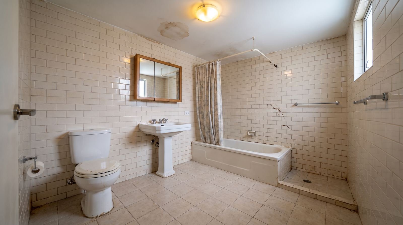 Baño antes de la reforma: azulejos gastados, bañera y humedad en el techo